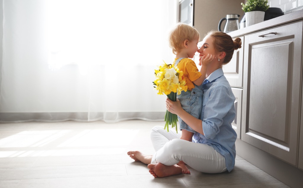 A woman and child sitting on the floor holding flowers.