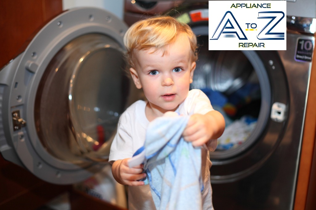A young child holding a white towel in front of an open dryer.